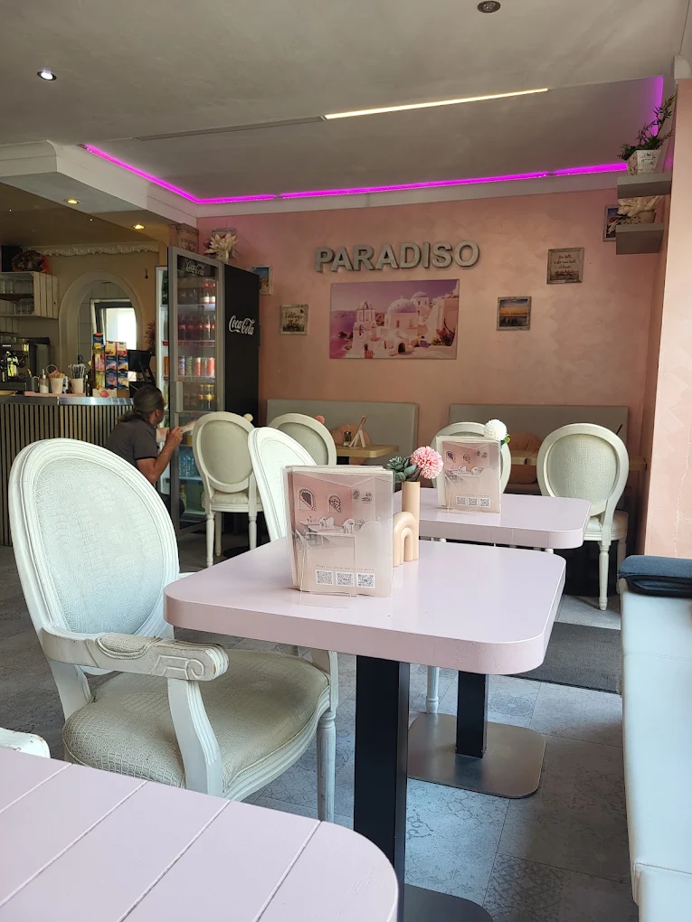 Gastraum des Café Paradiso mit rosa Tischen, weißen Stühlen und Neonlicht
